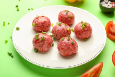 Plate with raw meat balls and cut green onion on color background, closeup