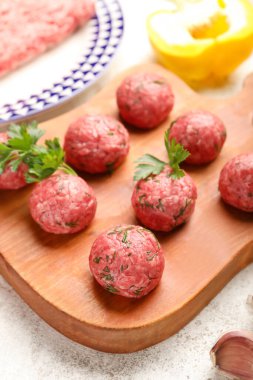 Cutting board with raw meat balls and herbs on light background