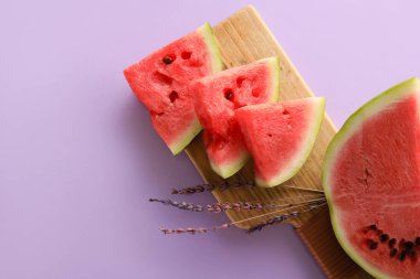 Cutting board with slices of watermelon and flowers on violet background