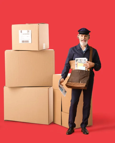 Handsome old postman and many big parcels on red background