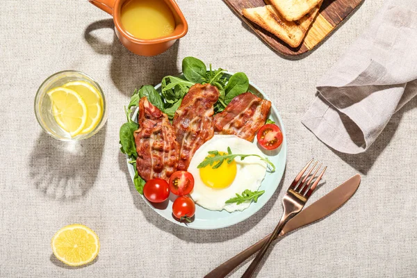 Plate with tasty fried egg, bacon and glass of water on fabric background