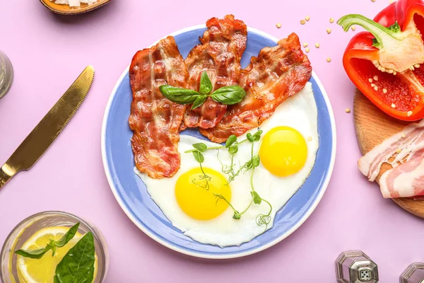 Plate of tasty fried eggs and bacon on pink background