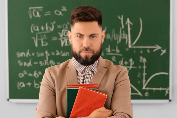 Handsome Math teacher with books in classroom