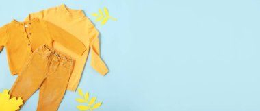 Yellow autumn baby clothes on blue background with space for text