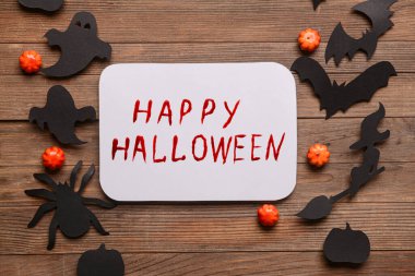 Paper sheet with text HAPPY HALLOWEEN and decor on wooden background