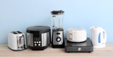 Different household appliances on table against light blue background 