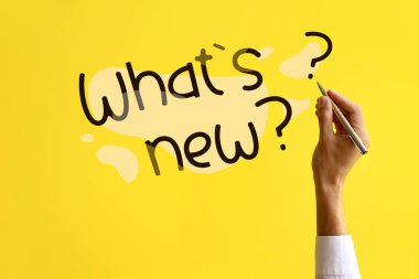 Man with pen writing text WHAT'S NEW? on yellow background