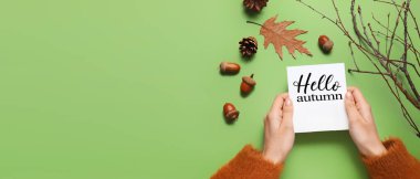 Woman holding card with text HELLO AUTUMN and floral decor on green background with space for text