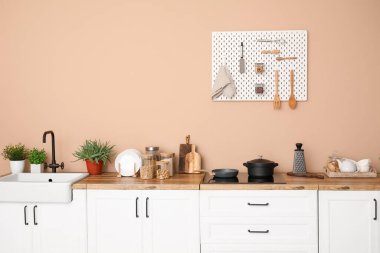 Interior of stylish kitchen with white counters, utensils and pegboard