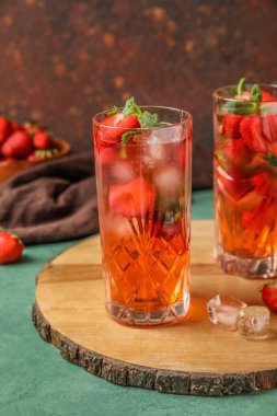 Board with glasses of strawberry lemonade on green table, closeup