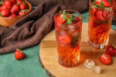Board with glasses of strawberry lemonade on green background