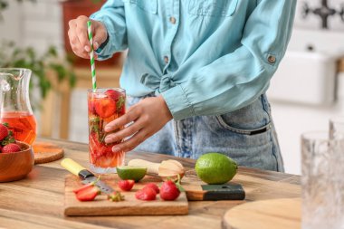 Woman with glass of cold strawberry lemonade in kitchen