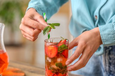 Woman putting mint into glass of strawberry lemonade, closeup
