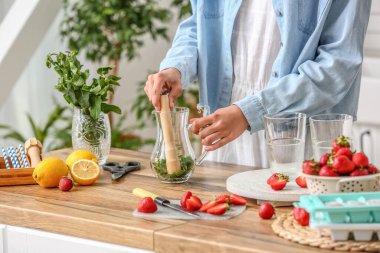 Woman preparing tasty strawberry lemonade on kitchen counter