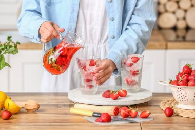 Woman pouring tasty strawberry lemonade into glass in kitchen