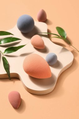 Stand with makeup sponges and plant leaves on beige background