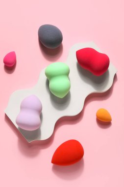 Stand with colorful makeup sponges on pink background