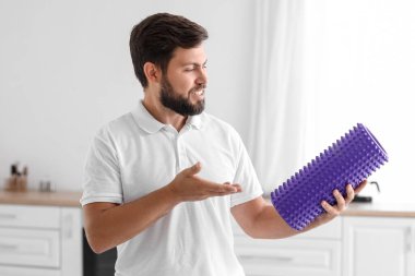 Young man with foam roller in kitchen