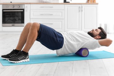 Young man training with foam roller in kitchen