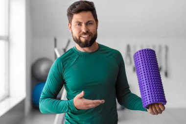 Handsome young man with foam roller in gym