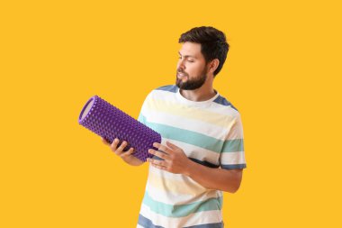 Young man with foam roller on yellow background