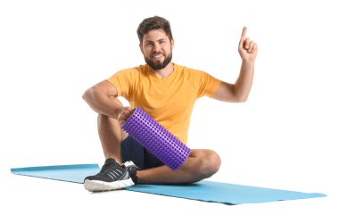 Young man with foam roller pointing at something on white background