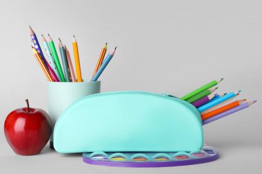 Blue case with pencils, paints and apple on grey background
