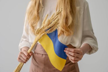Young woman with flag of Ukraine and spikelets on light background, closeup