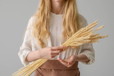 Young woman with wheat ears on light background, closeup