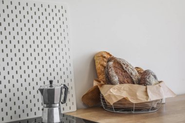 Basket with loaves of fresh bread and parchment paper on kitchen counter near light wall