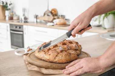 Woman cutting fresh bread at counter in kitchen, closeup