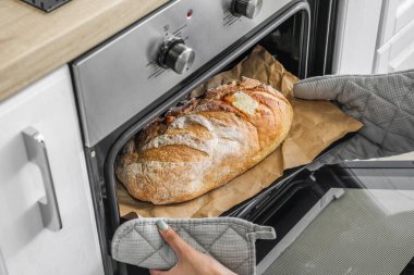 Woman taking baking sheet with bread from oven in kitchen, closeup