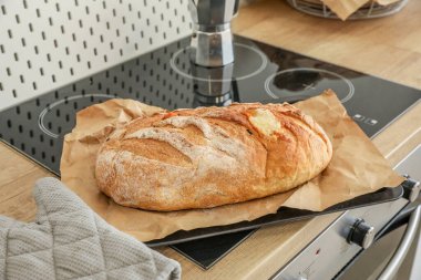 Baking sheet with fresh bread on stove in kitchen