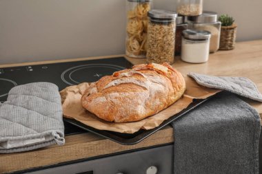 Baking sheet with fresh bread and parchment paper on stove in kitchen