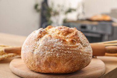 Cutting board with fresh bread on table in kitchen, closeup