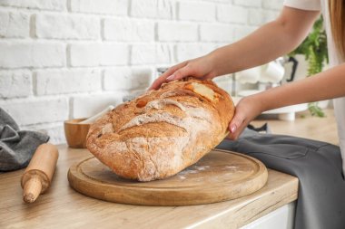 Woman taking fresh bread from board in kitchen, closeup