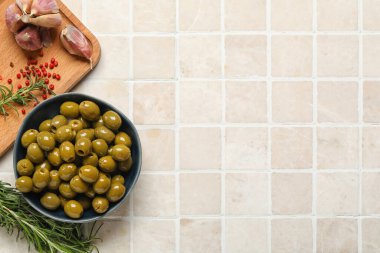 Bowl of tasty green olives, garlic, rosemary and peppercorns on light tile