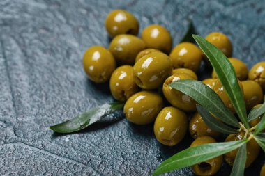 Heap of tasty green olives with leaves on dark color background, closeup