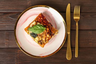 Plate of tasty Italian pie with mozzarella, pesto sauce and cutlery on wooden background