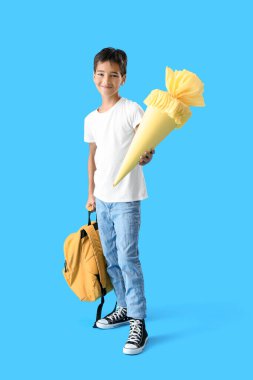 Little boy with yellow school cone and backpack on blue background