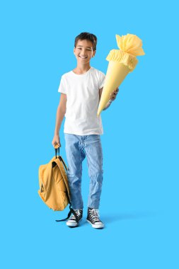 Little boy with yellow school cone and backpack on blue background