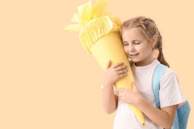 Cute little girl with yellow school cone on beige background