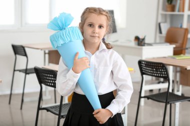 Cute little girl with blue school cone in classroom