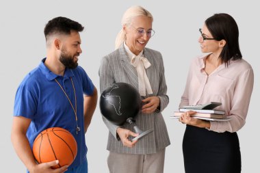 Teachers with ball, books and globe on light background