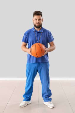 Handsome PE teacher with ball near light wall