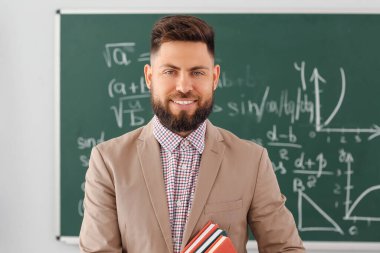 Handsome Math teacher with books in classroom