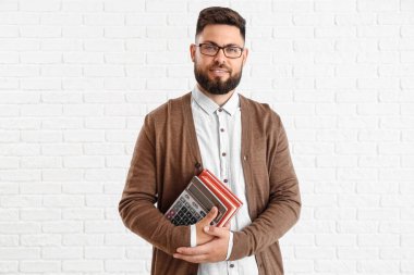 Handsome Math teacher with calculator and books on white brick background