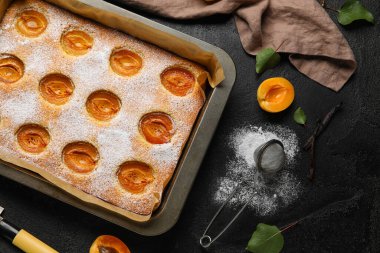 Baking tray with tasty apricot pie and sugar powder on dark background