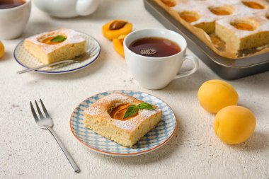 Plates with pieces of tasty apricot pie and tea on light background
