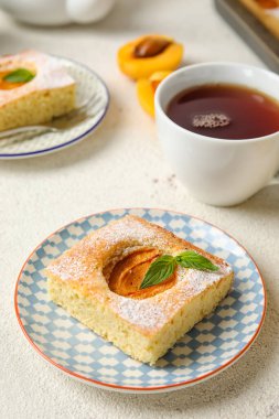 Plate with piece of tasty apricot pie and tea on light background
